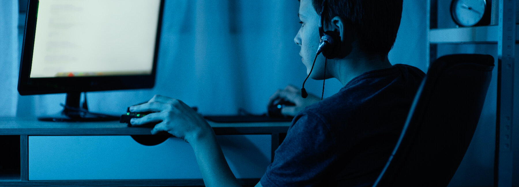 Kind zit met een headset aan een computer in een verduisterde kamer.