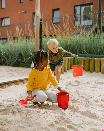 Kinderen spelen en bouwen met zand in een zandbak van de buitenschoolse opvang.