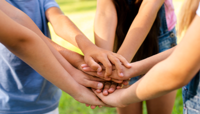 Groep kinderen legt de handen samen tijdens een activiteit in openlucht.