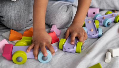 Kinderhanden spelen met houten voertuigen en blokken in verschillende kleuren.