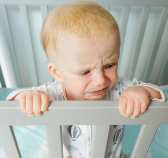 Baby staat recht in een babybedje en houdt de rand van het bed vast.