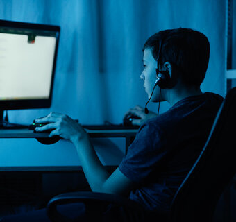Kind zit met een headset aan een computer in een verduisterde kamer.