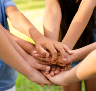 Groep kinderen legt de handen samen tijdens een activiteit in openlucht.