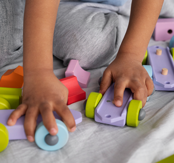 Kinderhanden spelen met houten voertuigen en blokken in verschillende kleuren.